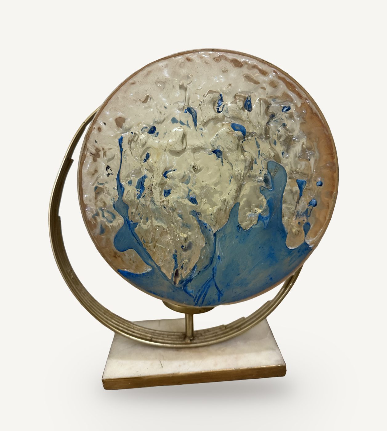 Ocean, by Accident: a round epoxy disc painted with blue and cream wave forms, held in a brass globe stand on a marble base
