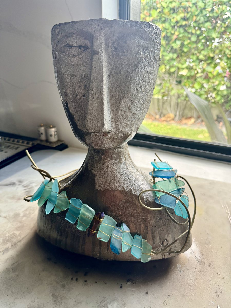 The Navigator: a gray cement head with a long face and a turquoise sea-glass necklace on bronze wire