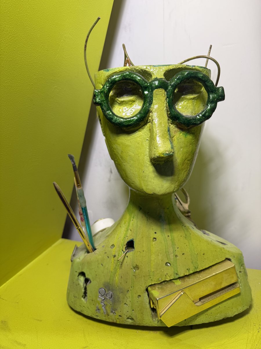 The Witness: a lime-green cast head with round green glasses, brushes and pencils tucked into it